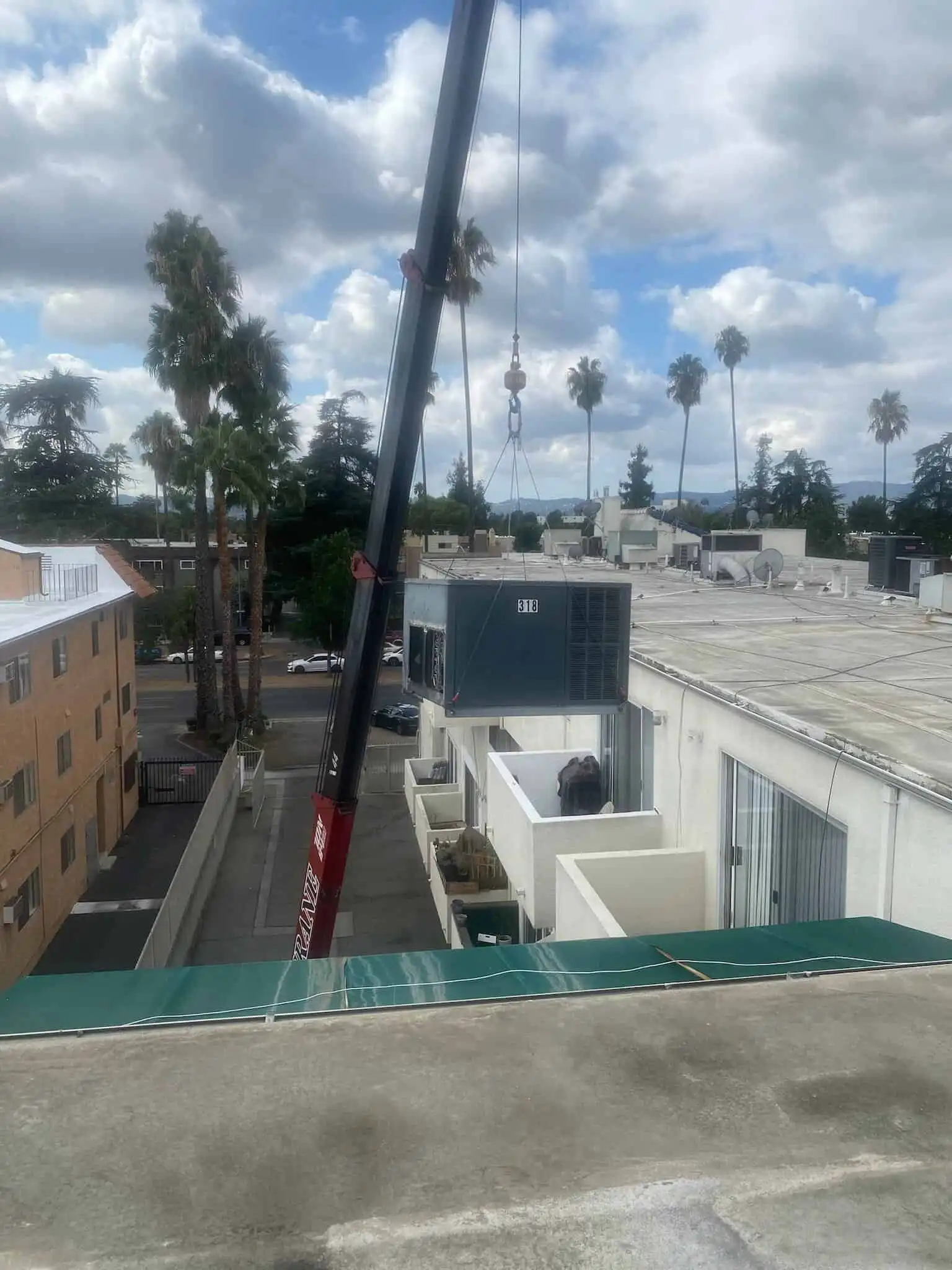 Crane lifting a rooftop AC unit onto a multi-story apartment building in Los Angeles