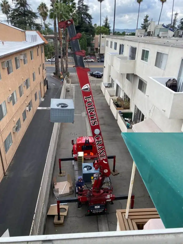 Crane lifting rooftop HVAC unit for installation at Los Angeles multi-family building