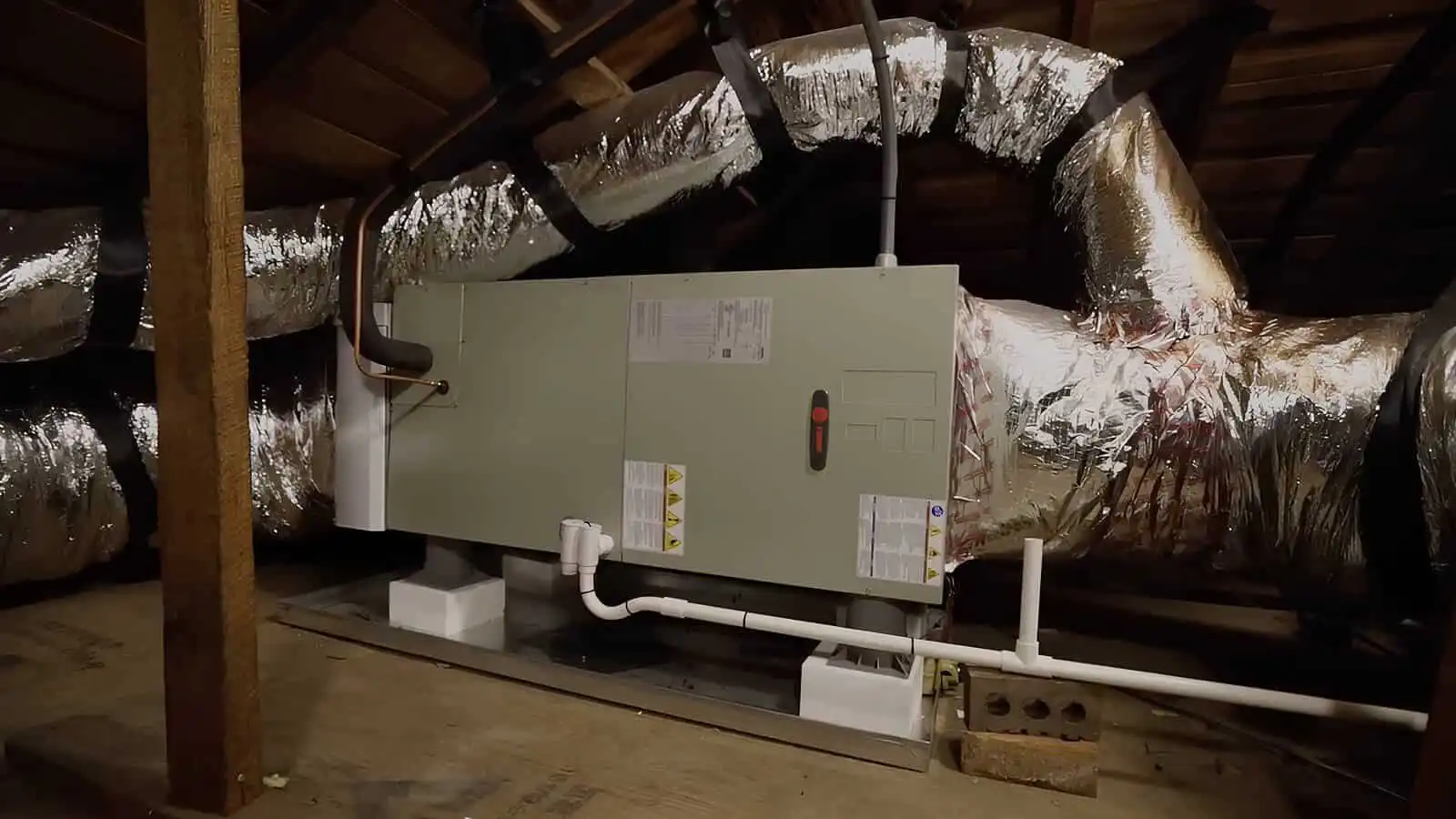 HVAC air handler unit installed in an attic space with ductwork and insulation.