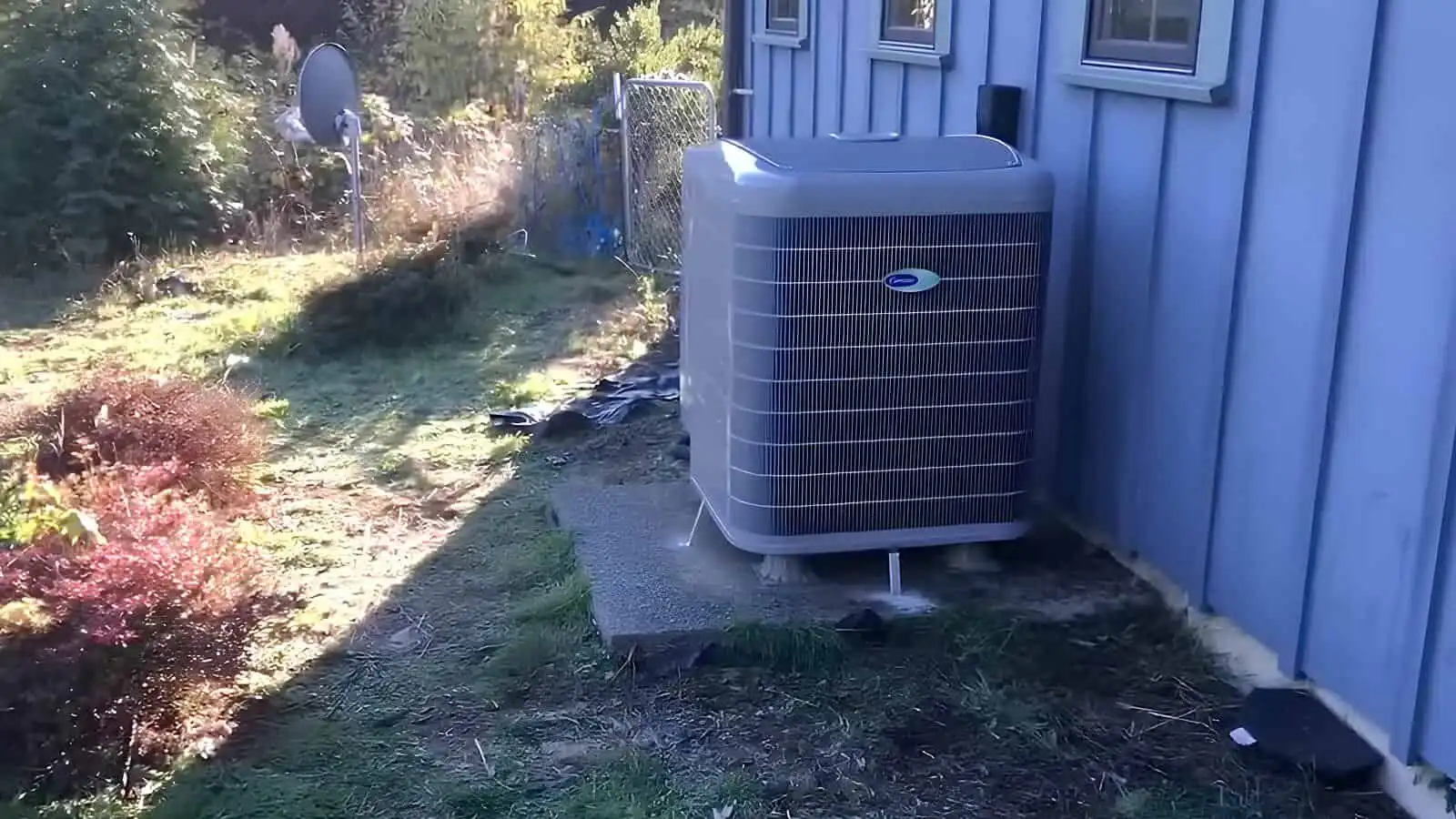 AC unit outside a blue house in a backyard, with trees and a satellite dish nearby.