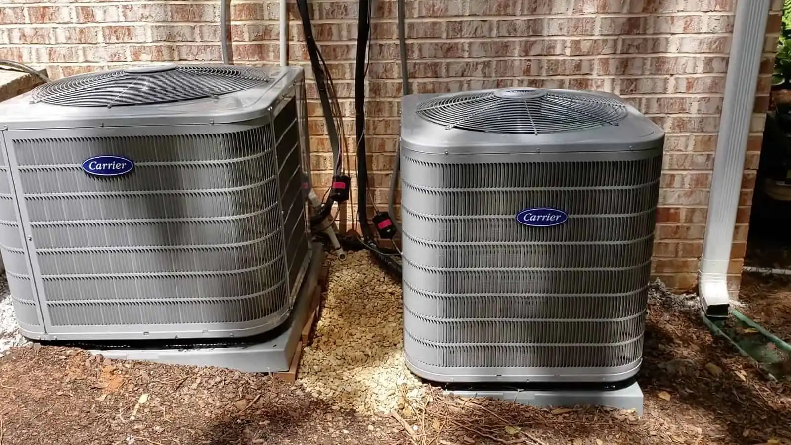 Two Carrier heat pump units installed outdoors against a brick wall.
