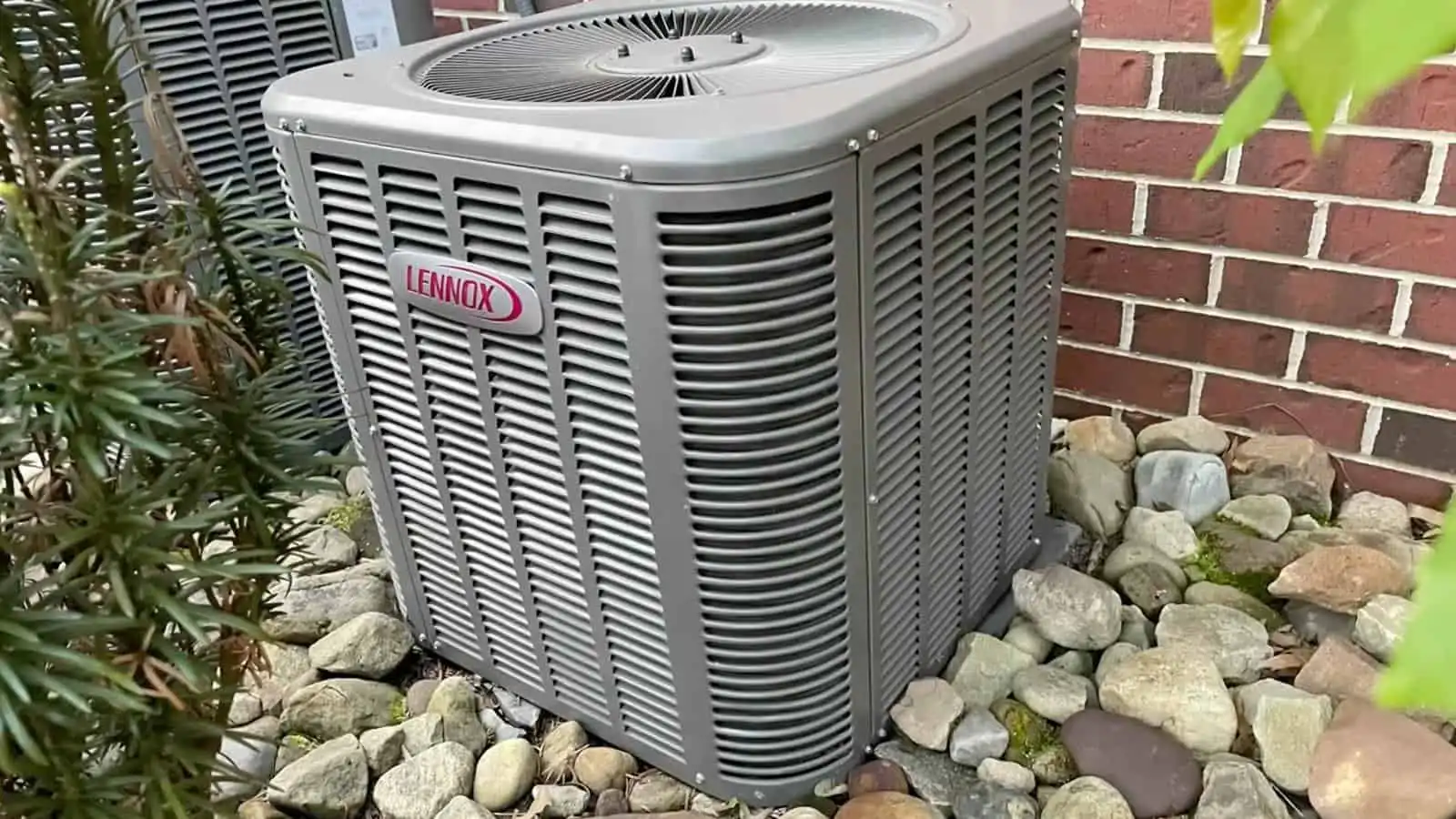 HVAC outdoor air conditioning unit on a concrete pad next to a brick wall.
