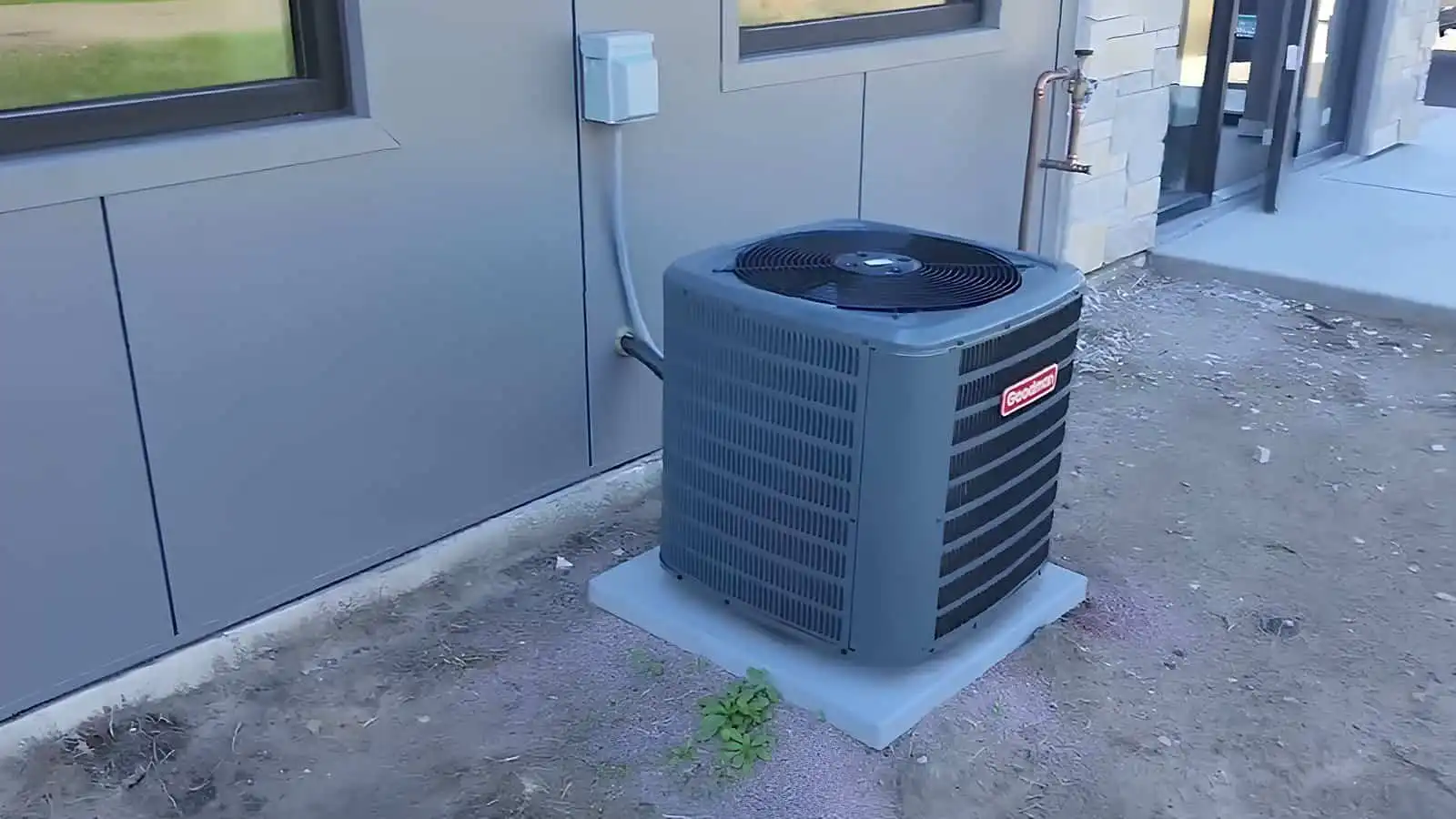 Air conditioning outdoor unit on concrete pad beside building wall.