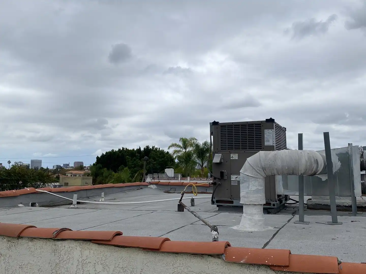 Rooftop package unit on a flat roof above a tile-roofed building