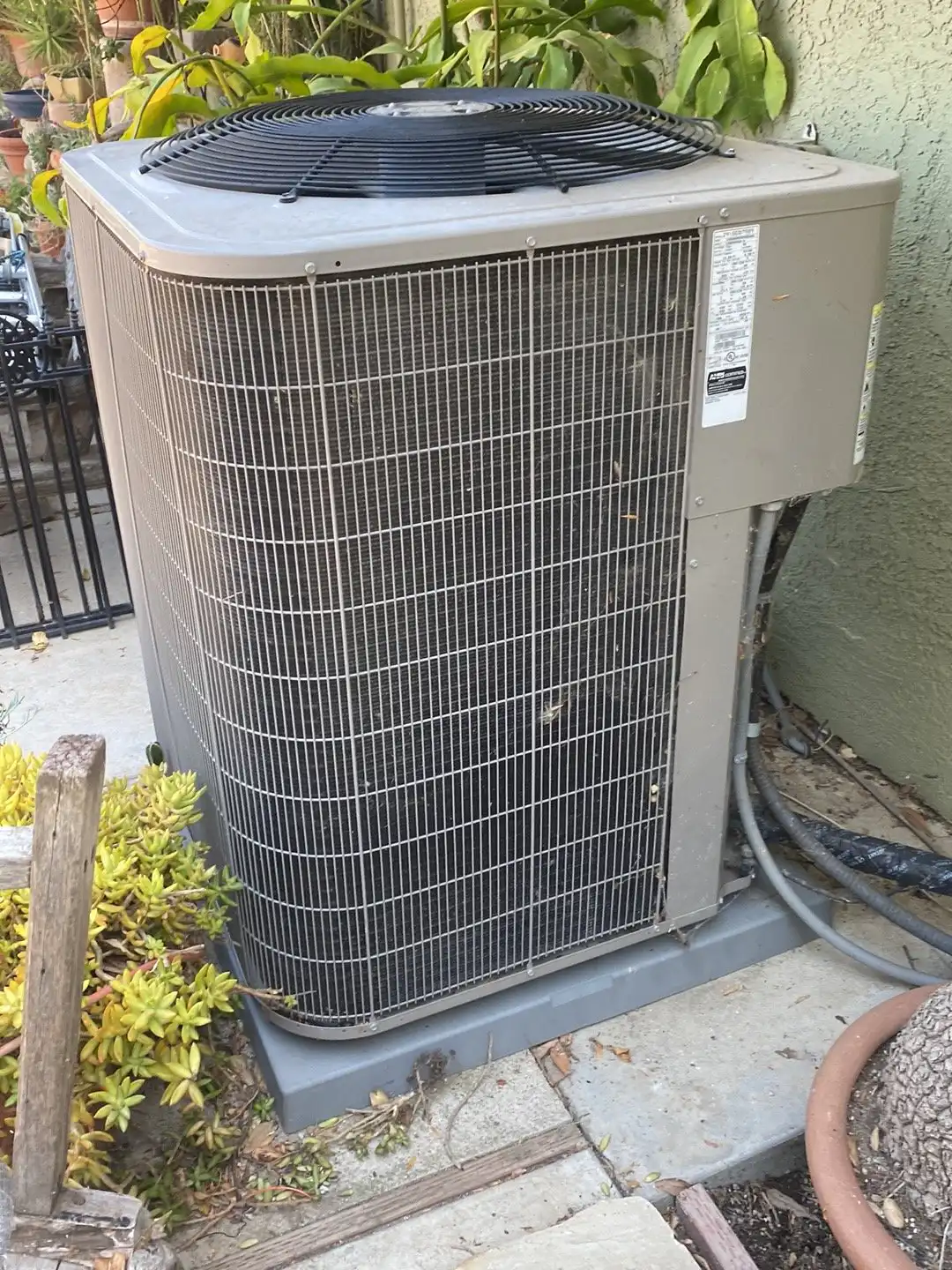 Older central AC condenser beside a stucco wall, the kind of system we diagnose on Sylmar repair calls