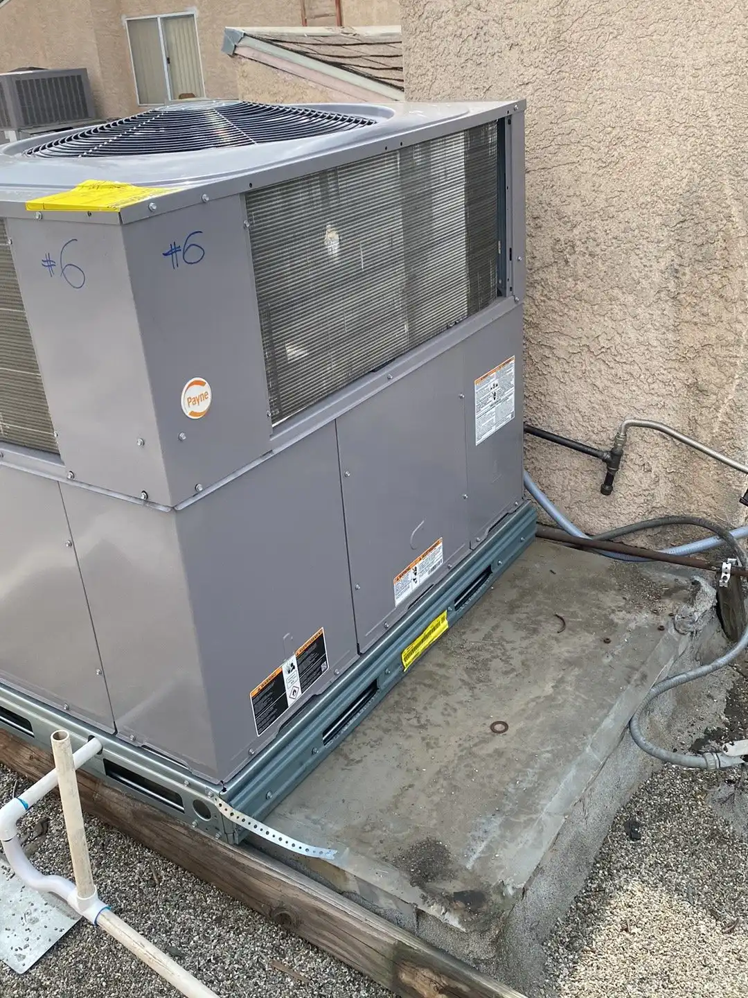 Packaged heating and cooling unit set on a concrete pad beside a stucco wall