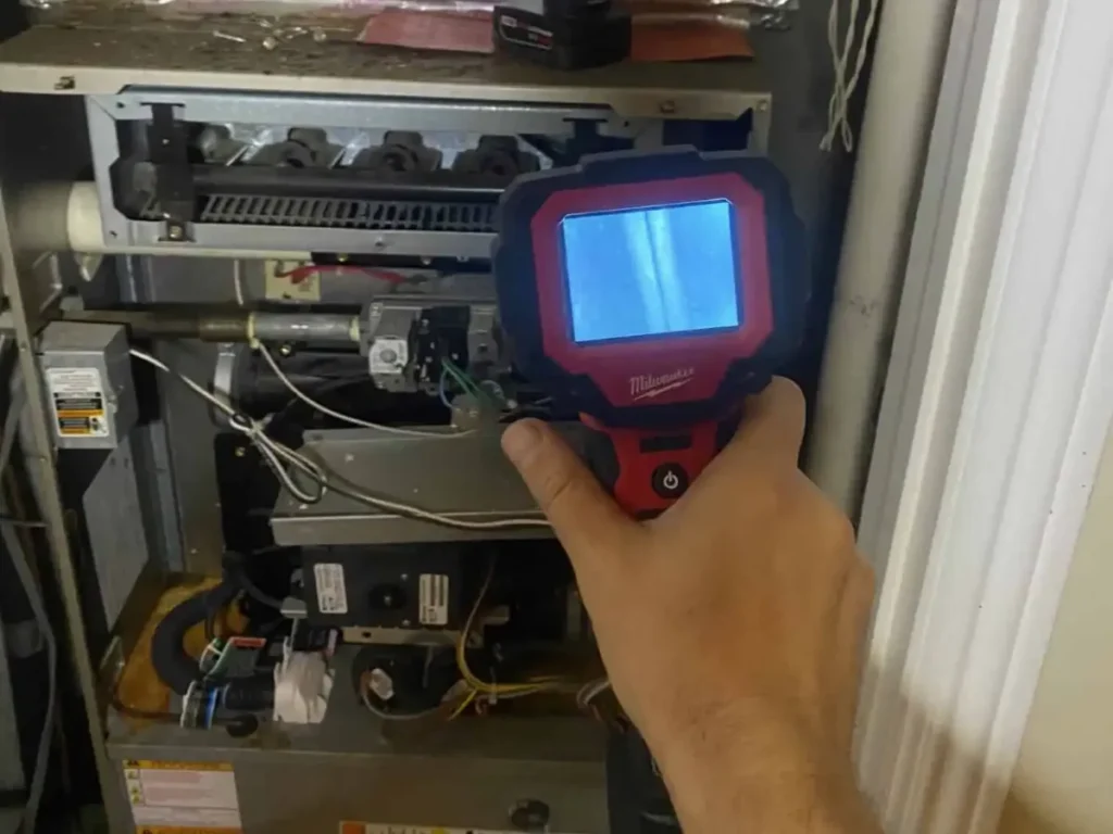 Handheld inspection camera aimed into the burner section of an open gas furnace
